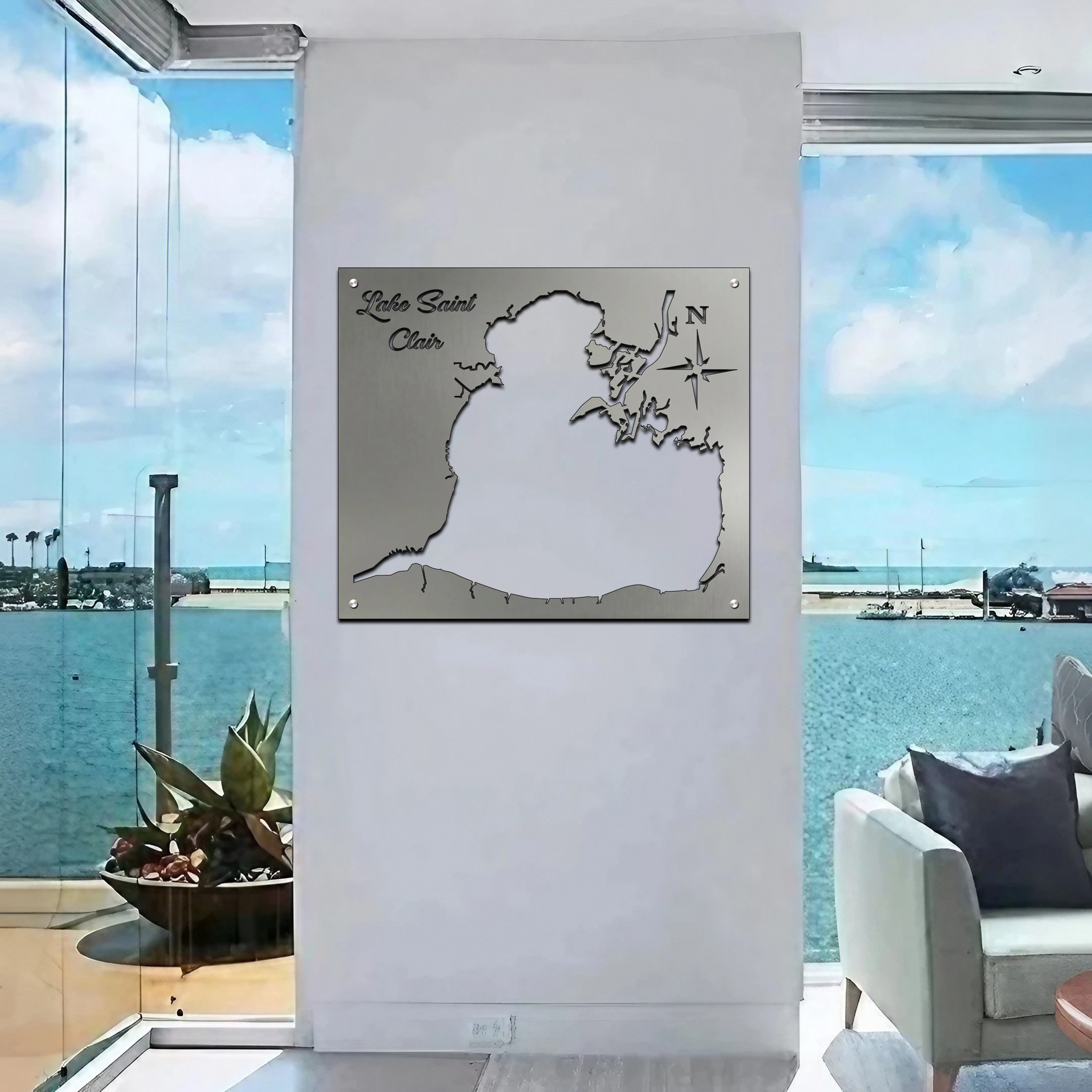 Metal map of Lake Saint Clair displayed on a wall, with a scenic view of water and plants outside.