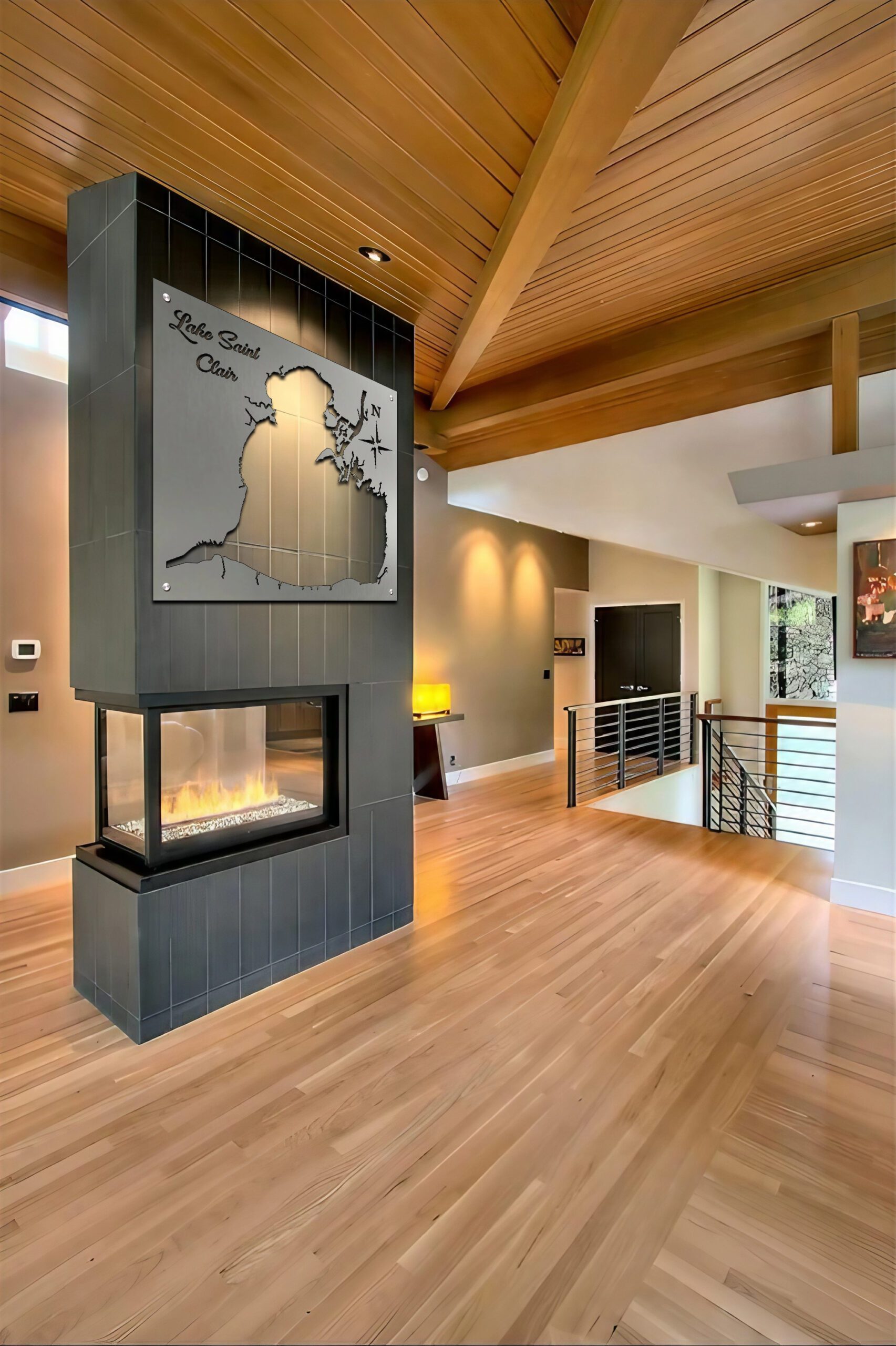 A modern living space features a fireplace with a Lake Saint Clair map above it, hardwood floors, and wooden beams.