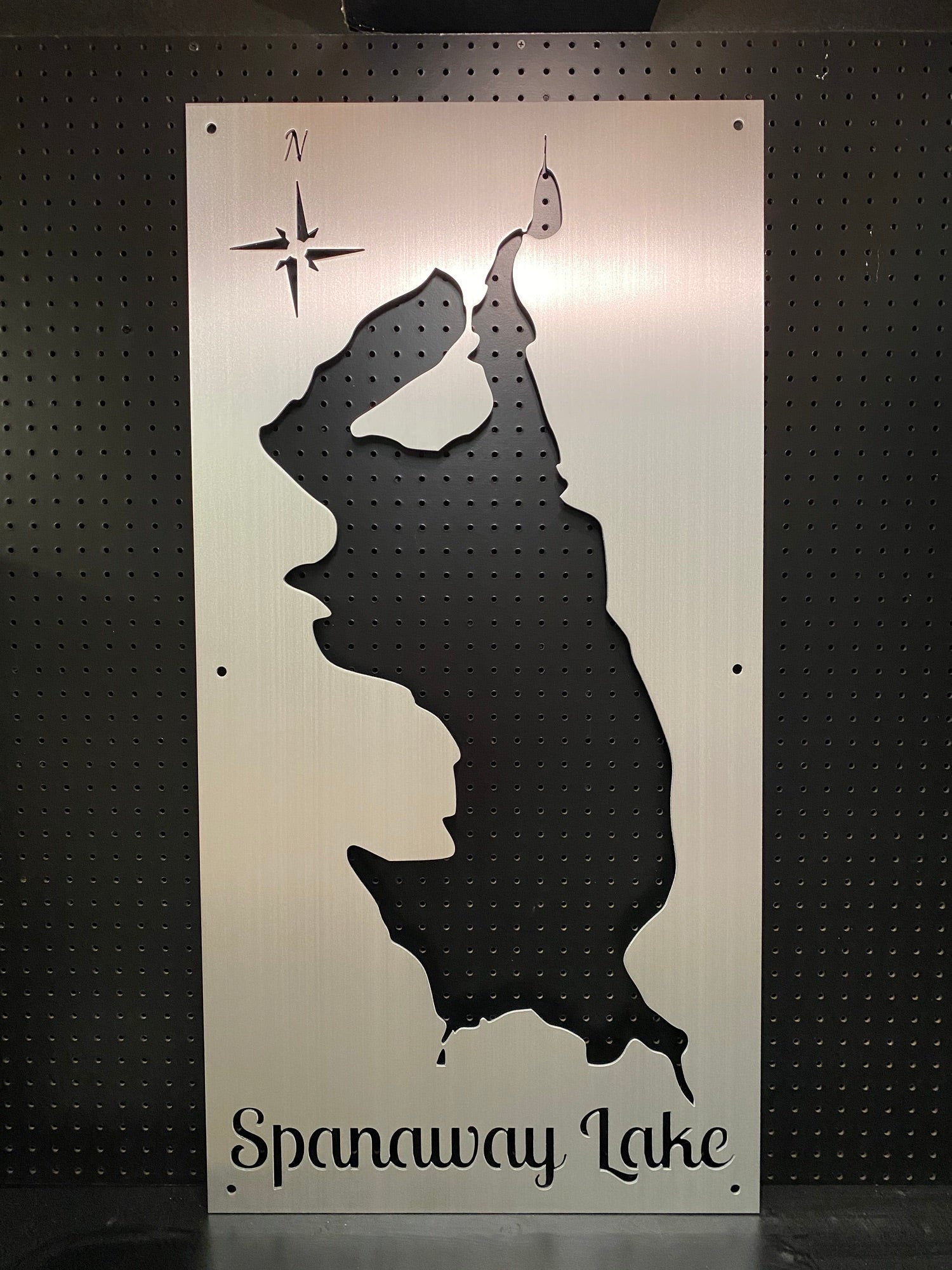 Spanaway Lake metal map with compass rose cutout, mounted on a black pegboard.