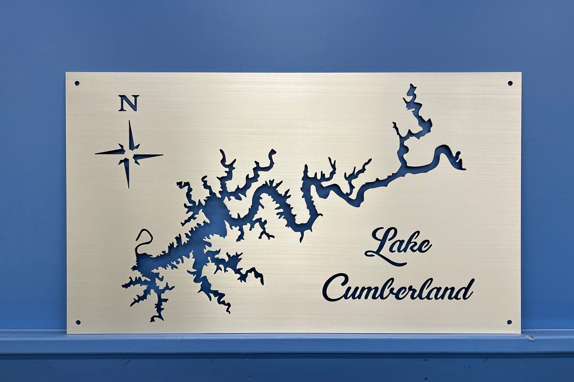 Lake Cumberland map on brushed metal with decorative script and compass rose, set against a blue wall.