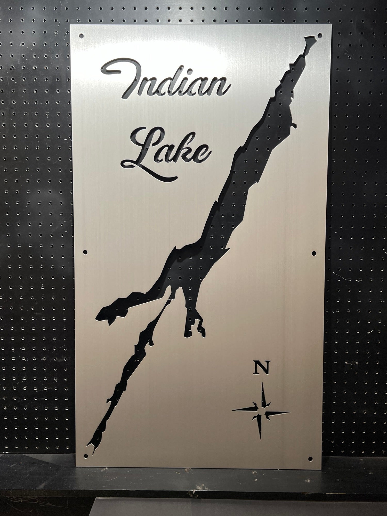 Metal map of Indian Lake with compass rose on a perforated black background.