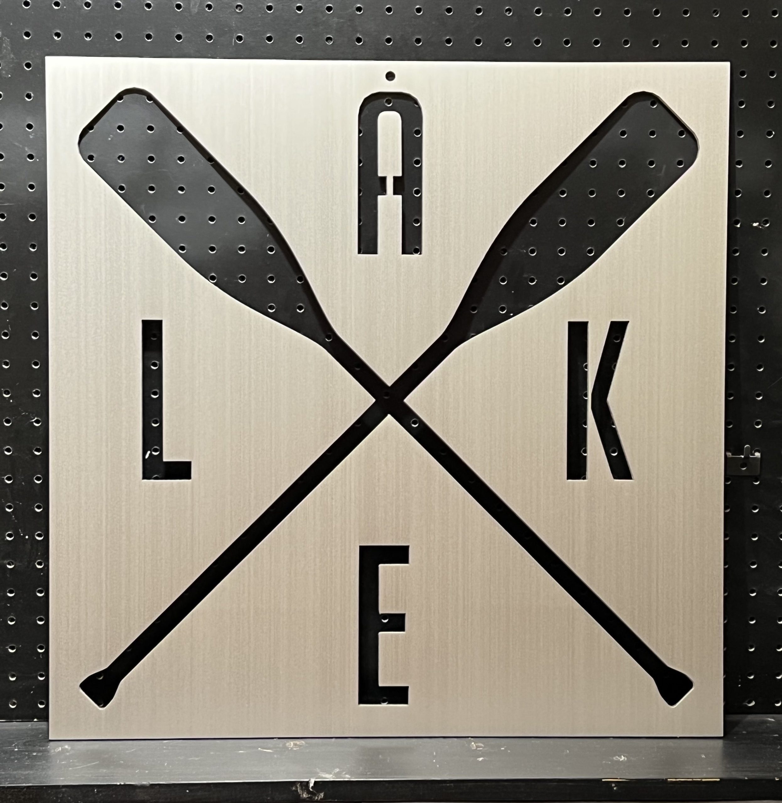 Custom metal sign with crossed oars and "LAKE" cutout on a brushed metallic background.