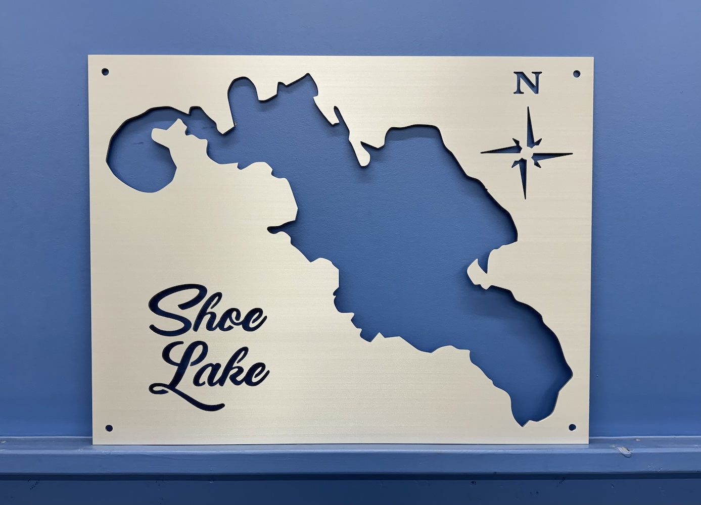 Shoe Lake metal map with compass rose on a blue wall background.