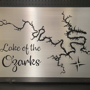 Lake of the Ozarks metal map sign with compass rose on brushed silver, mounted on a dark pegboard.