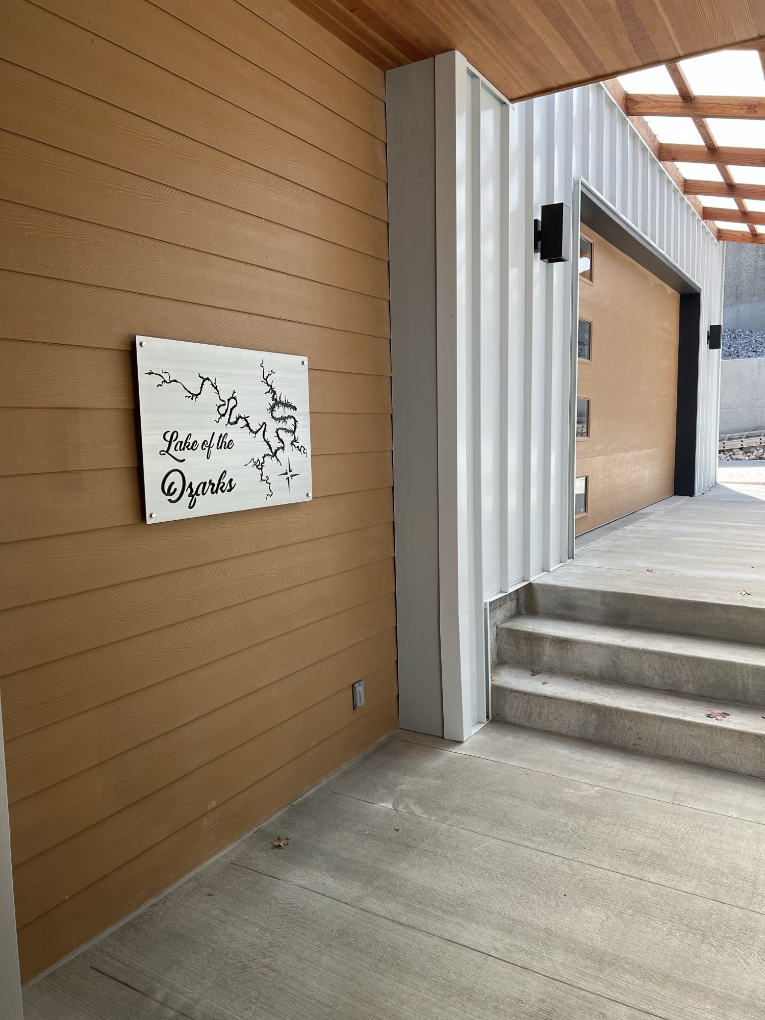 Lake of the Ozarks metal map sign on a tan wall, located near a modern garage entrance with concrete steps.