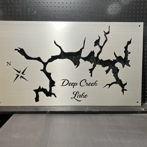 Metal map of Deep Creek Lake with compass rose, mounted on a perforated black background.