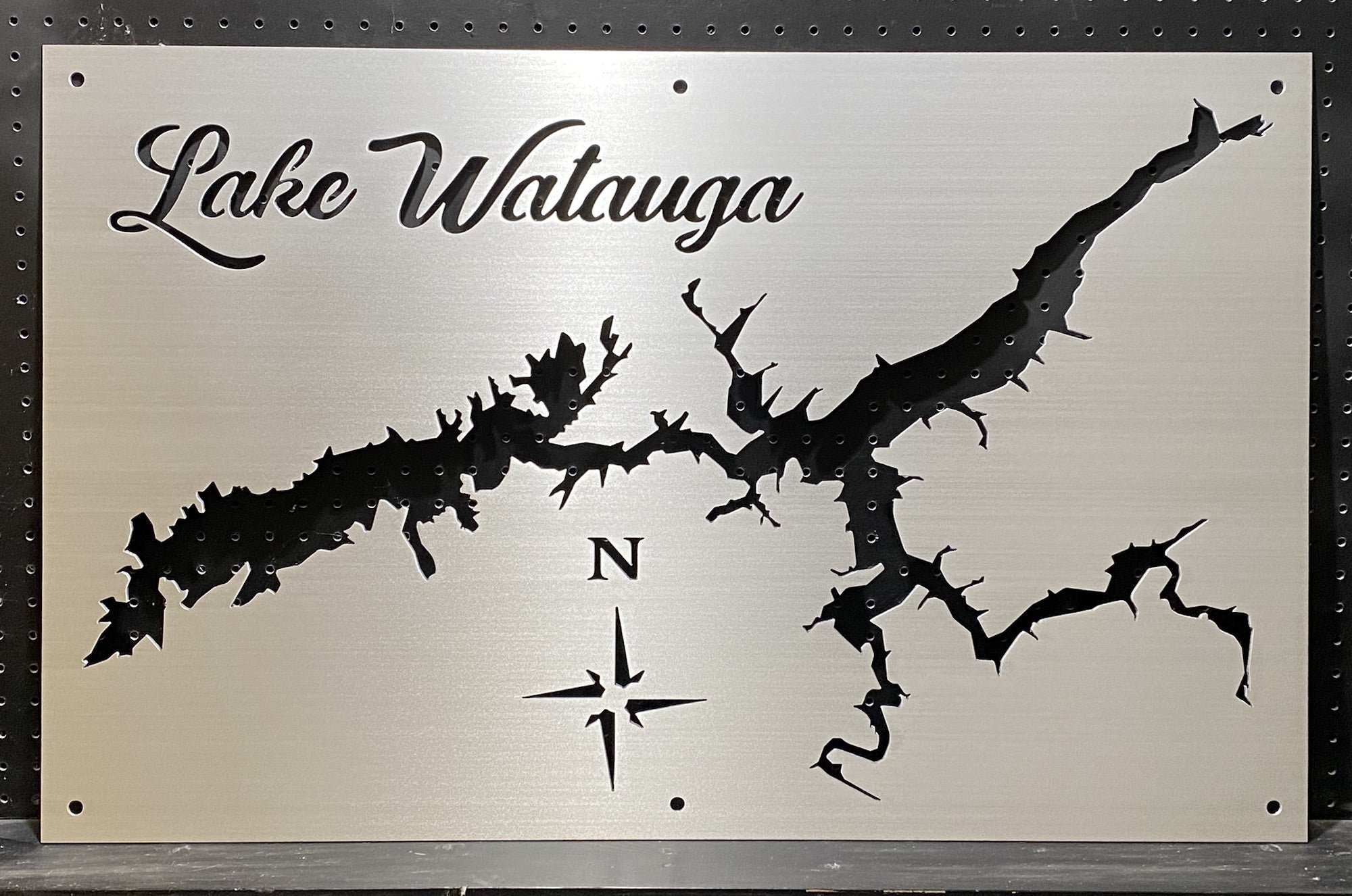 Lake Watauga metal map with compass rose, featuring detailed cutout design on brushed silver, mounted on a black pegboard.