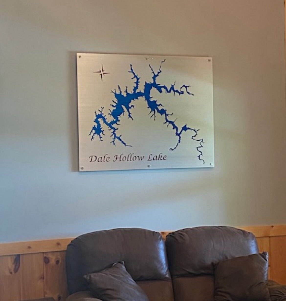 Metal map of Dale Hollow Lake with blue silhouette and compass rose, mounted above a couch on a light-colored wall.