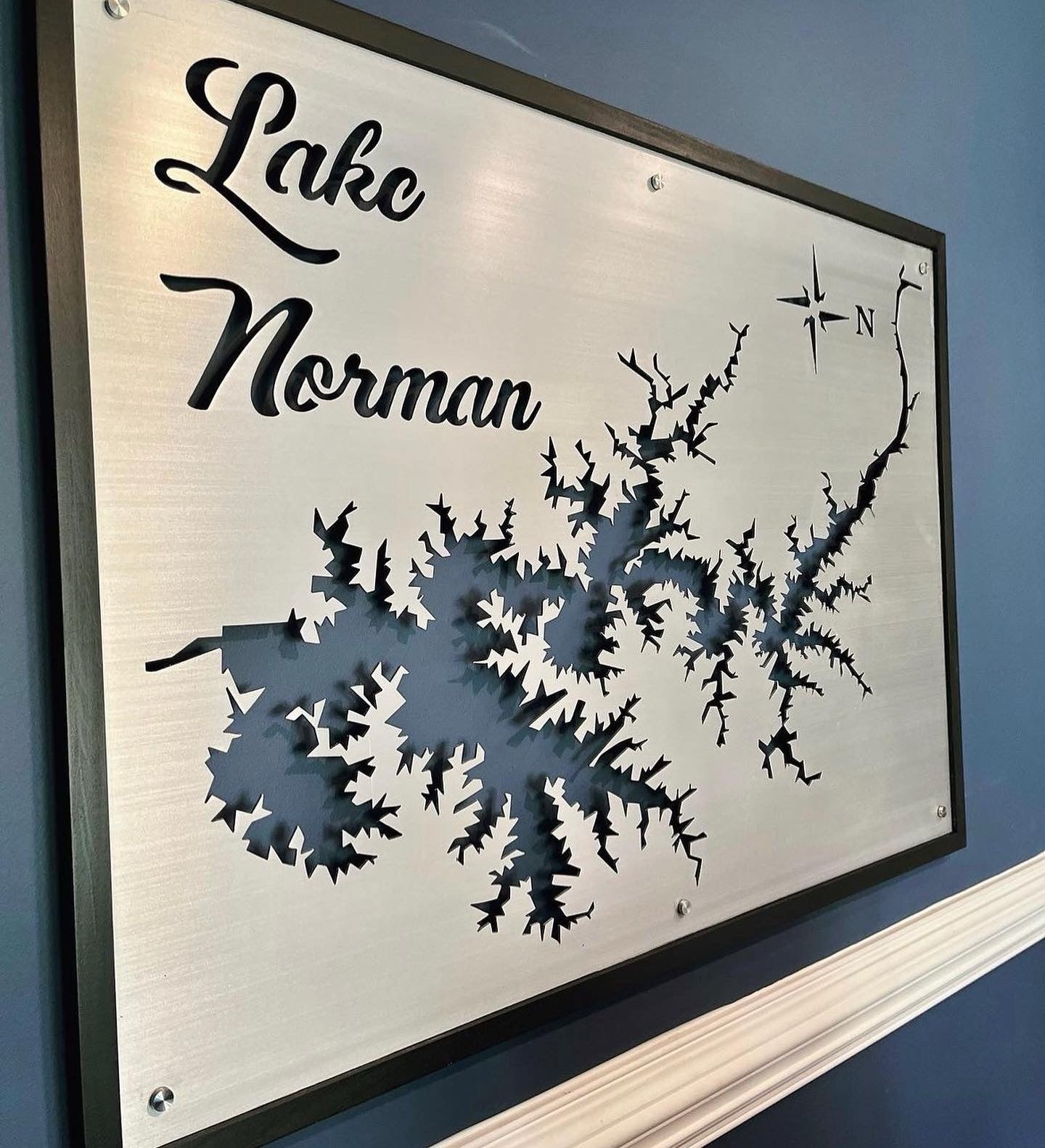 Lake Norman metal map with compass rose, mounted on a blue wall.