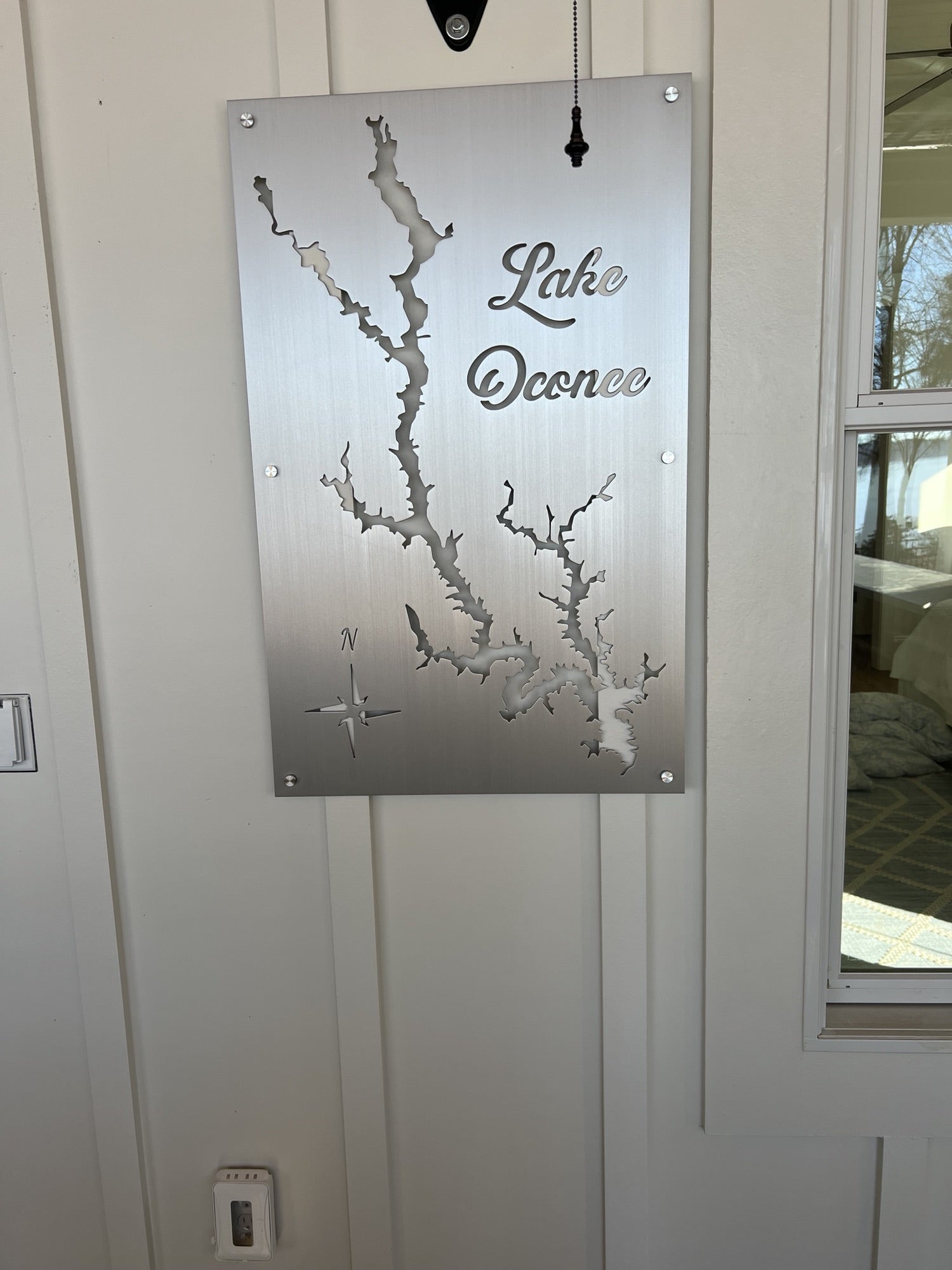 Lake Oconee metal map with compass rose detail, mounted on a light wall beside a window.