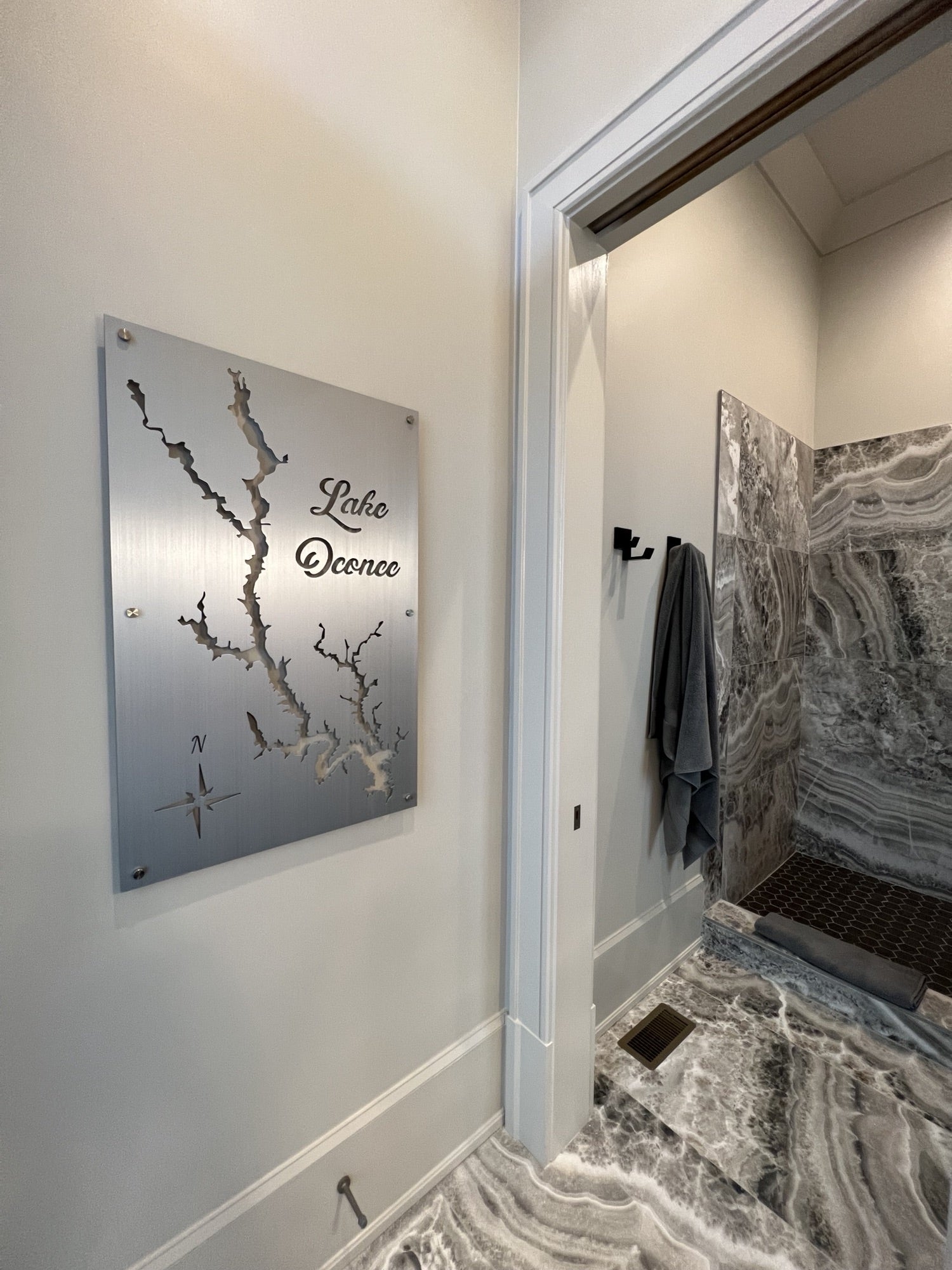 Lake Oconee metal map with compass rose detail on a light wall, adjacent to a marble-accented bathroom.