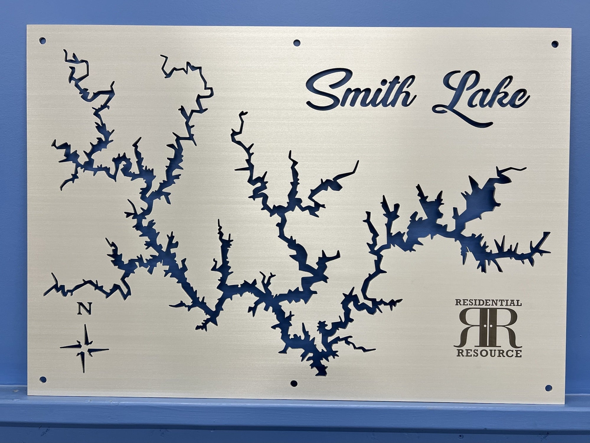 Smith Lake metal map with compass rose and "Residential Resource" logo on brushed silver, mounted on a blue wall.