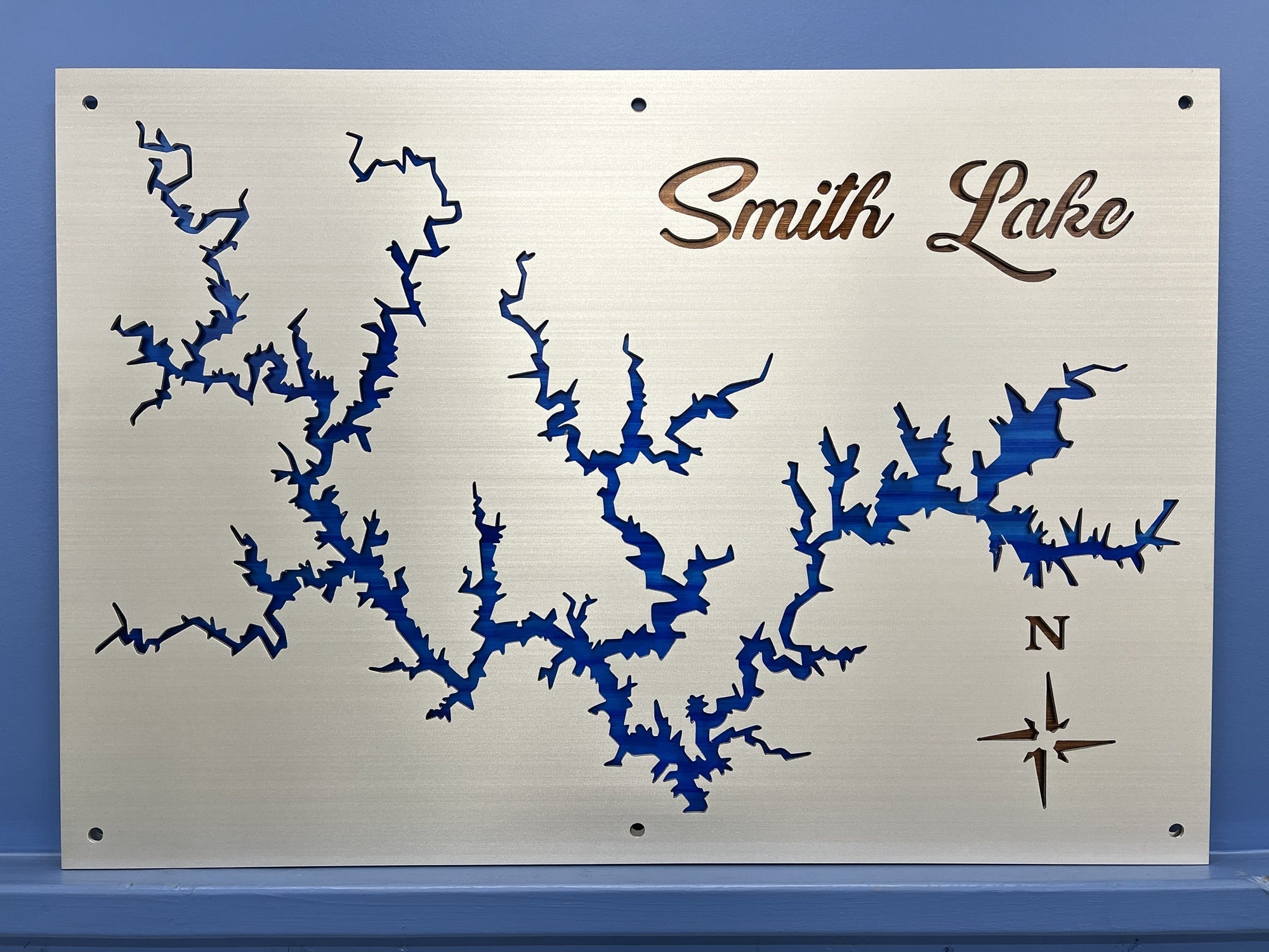 Smith Lake metal map with blue cutout design and compass rose, mounted on a blue wall.
