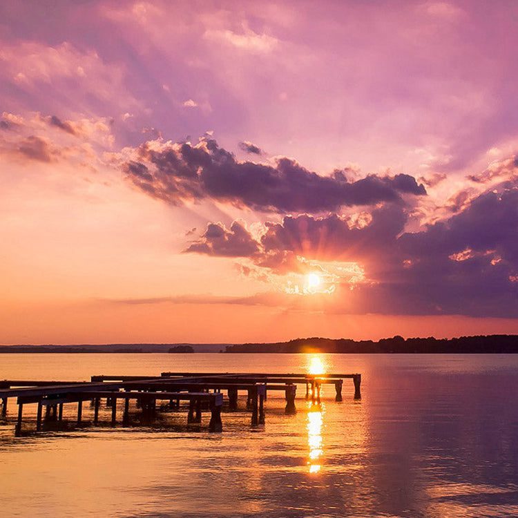 Purple sunset over a calm lake with clouds and a wooden pier reflecting on the water.