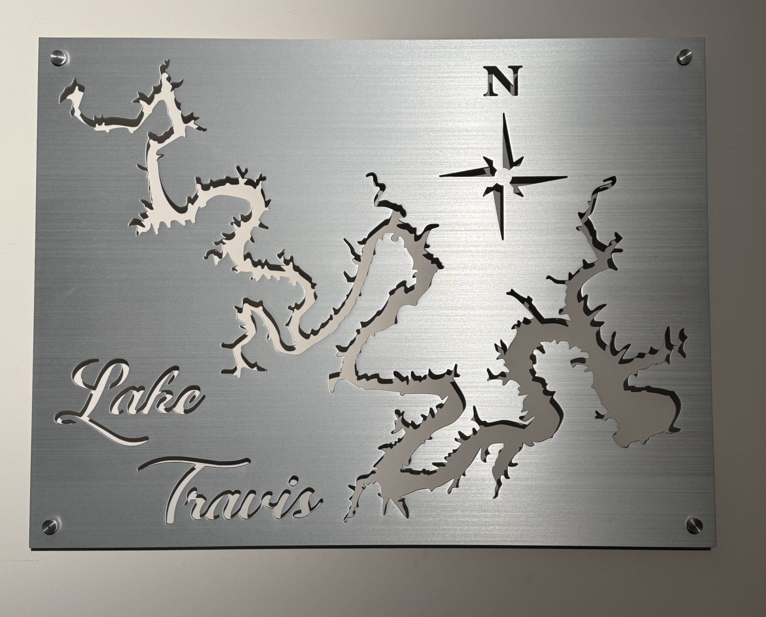 Metal wall art of Lake Travis with a compass rose and engraved text, featuring intricate lake outlines.