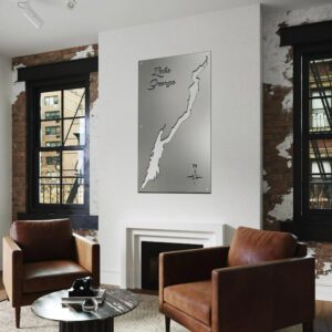 Metal map of Lake George displayed on a wall in a modern living room with brown chairs and a coffee table.