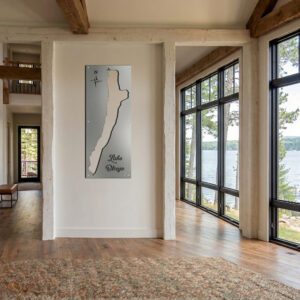 Metal map of Lake Otsego displayed on a wall in a bright, modern room with large windows overlooking the lake.