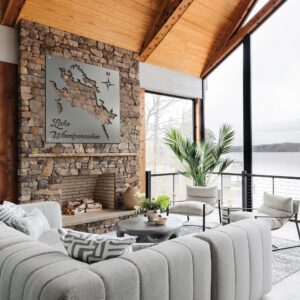 Metal map of Lake Winnipesaukee hangs above a stone fireplace in a modern living room with large windows.