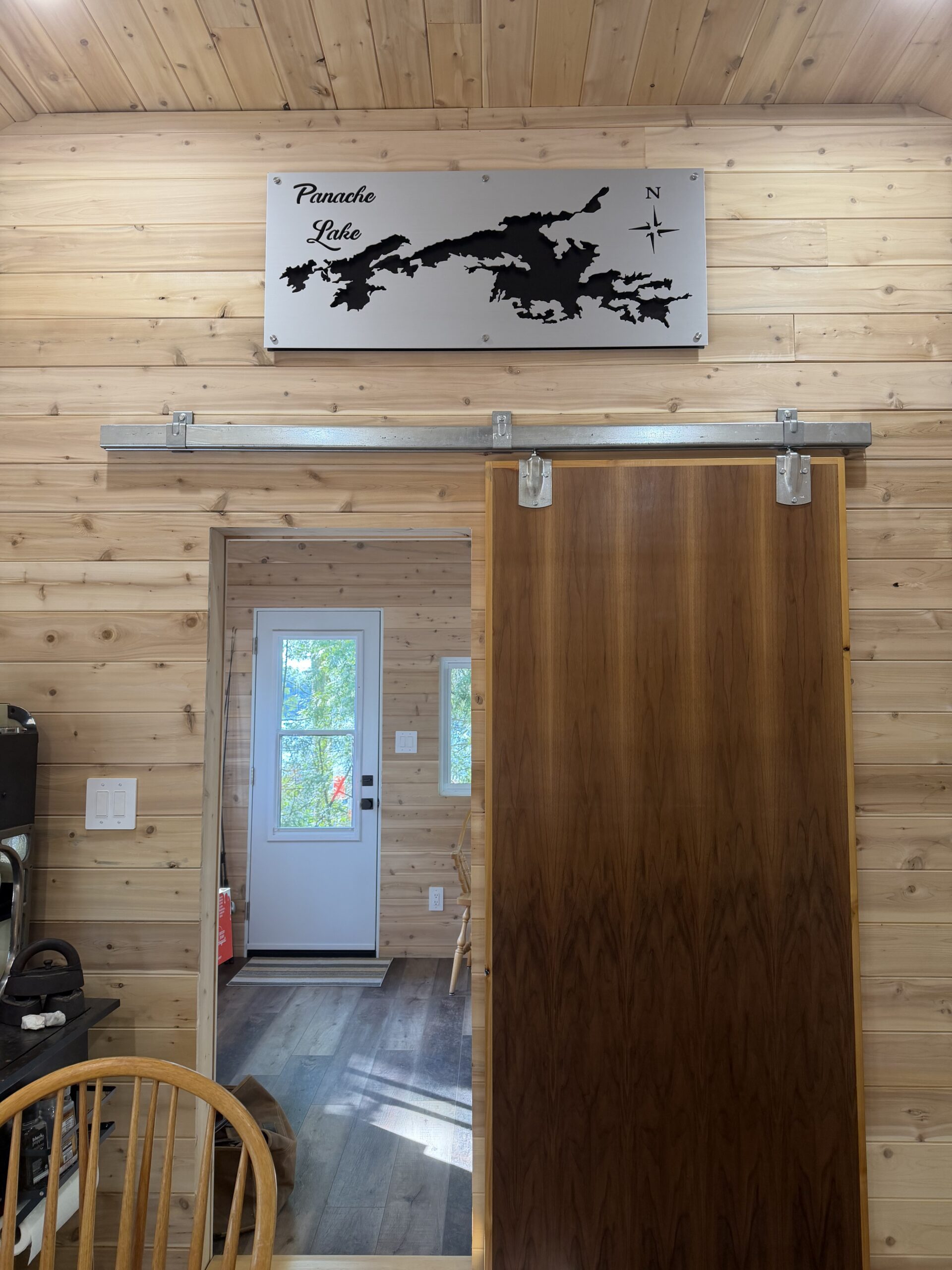 Metal map of Panache Lake mounted on a wooden wall, with a sliding door and visible entryway.