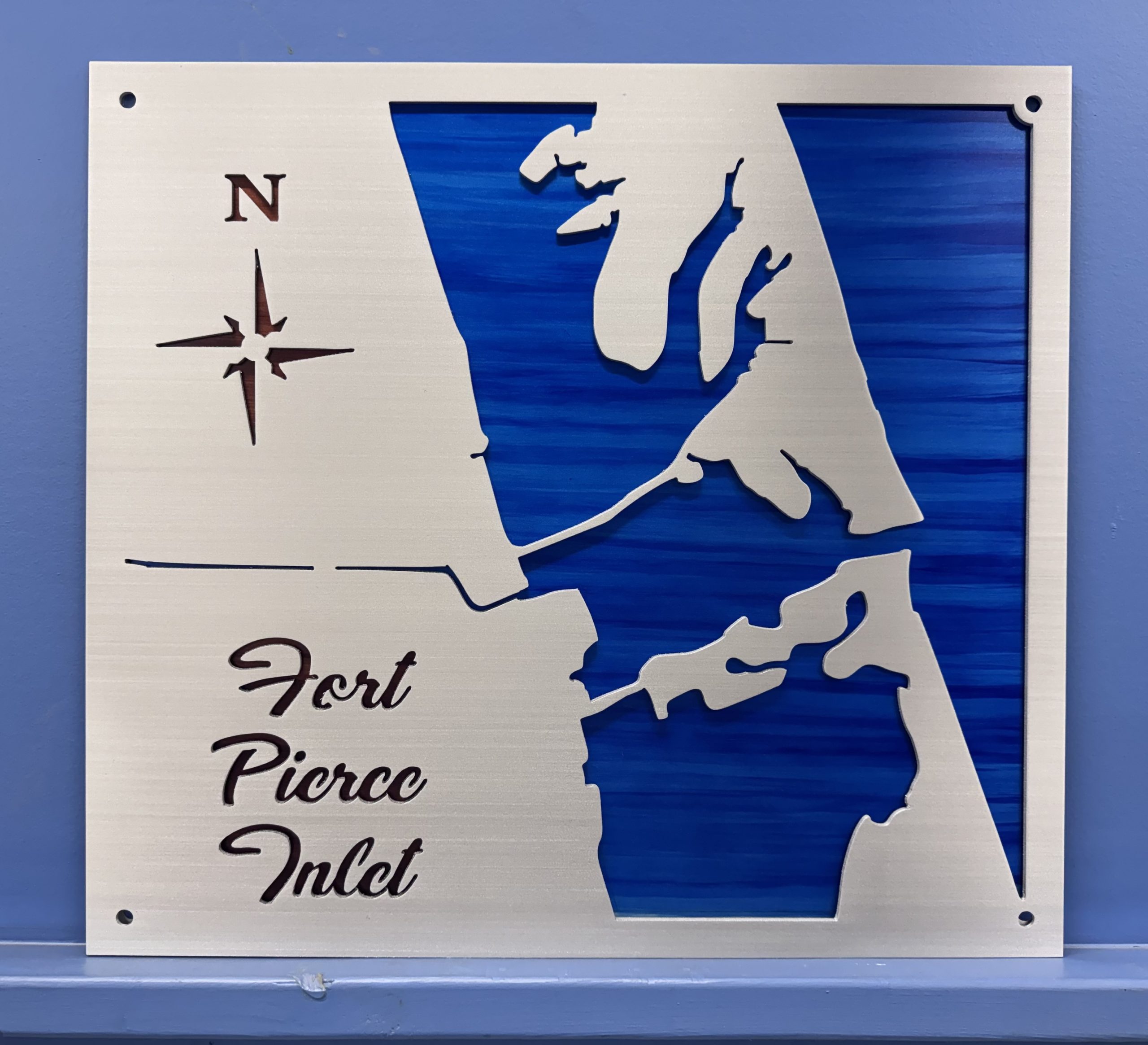 Metal map of Fort Pierce Inlet, featuring cut-out details and a blue background. North direction indicated.