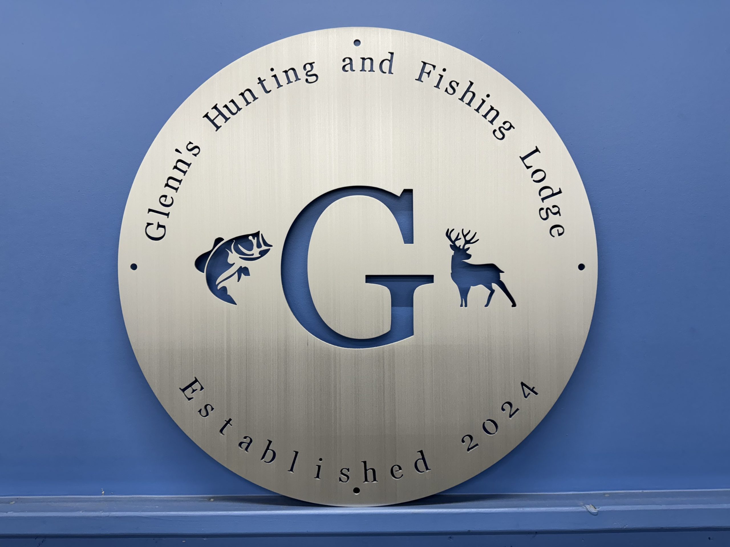 Custom round brushed metal sign for Glenn’s Hunting and Fishing Lodge, with open cutouts.