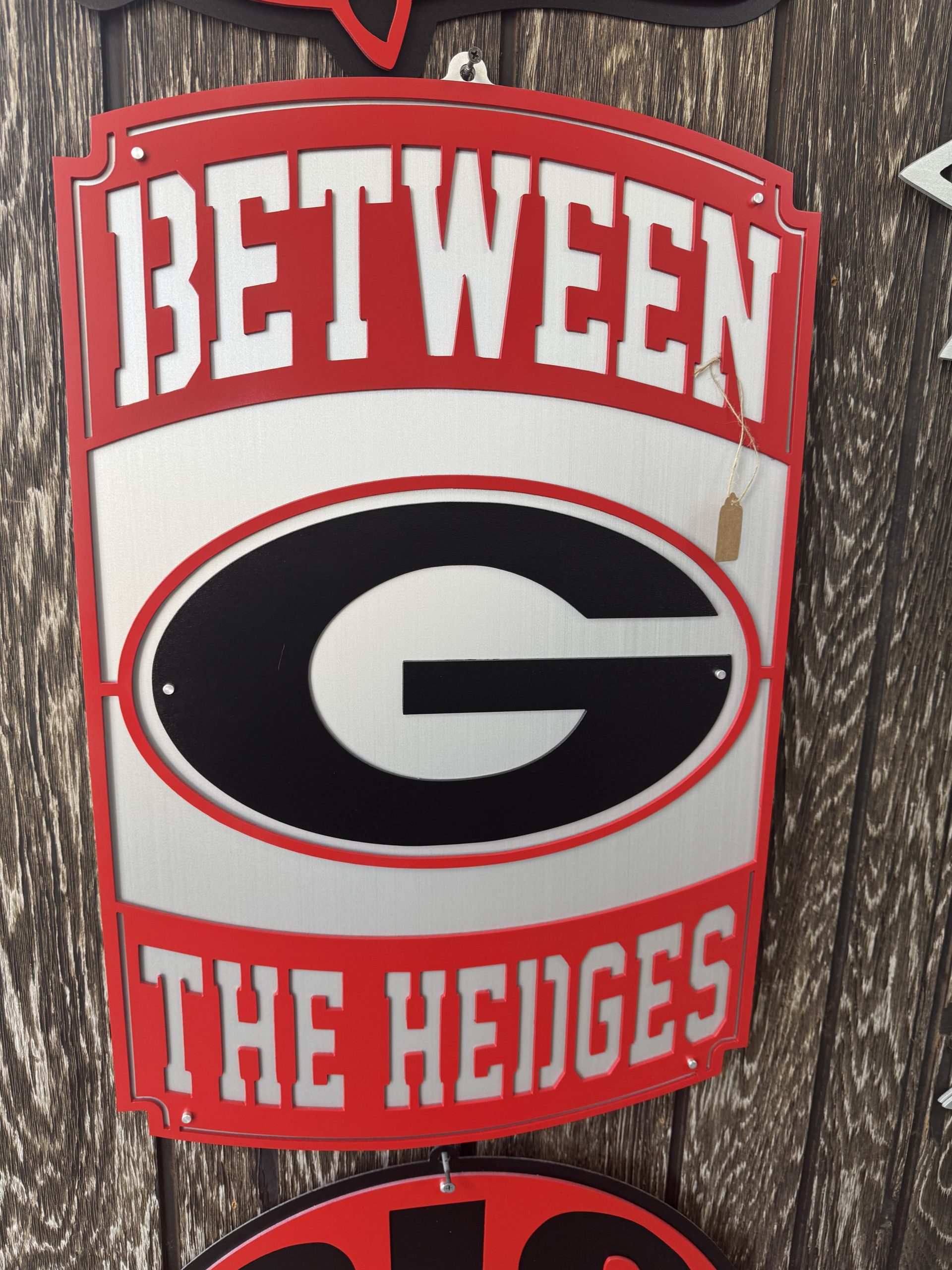 Custom red and black metal sign reading Between the Hedges.