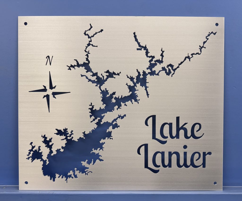 Lake Lanier brushed metal map with compass rose and open shoreline cutouts, shown without a backplate against a blue wall.