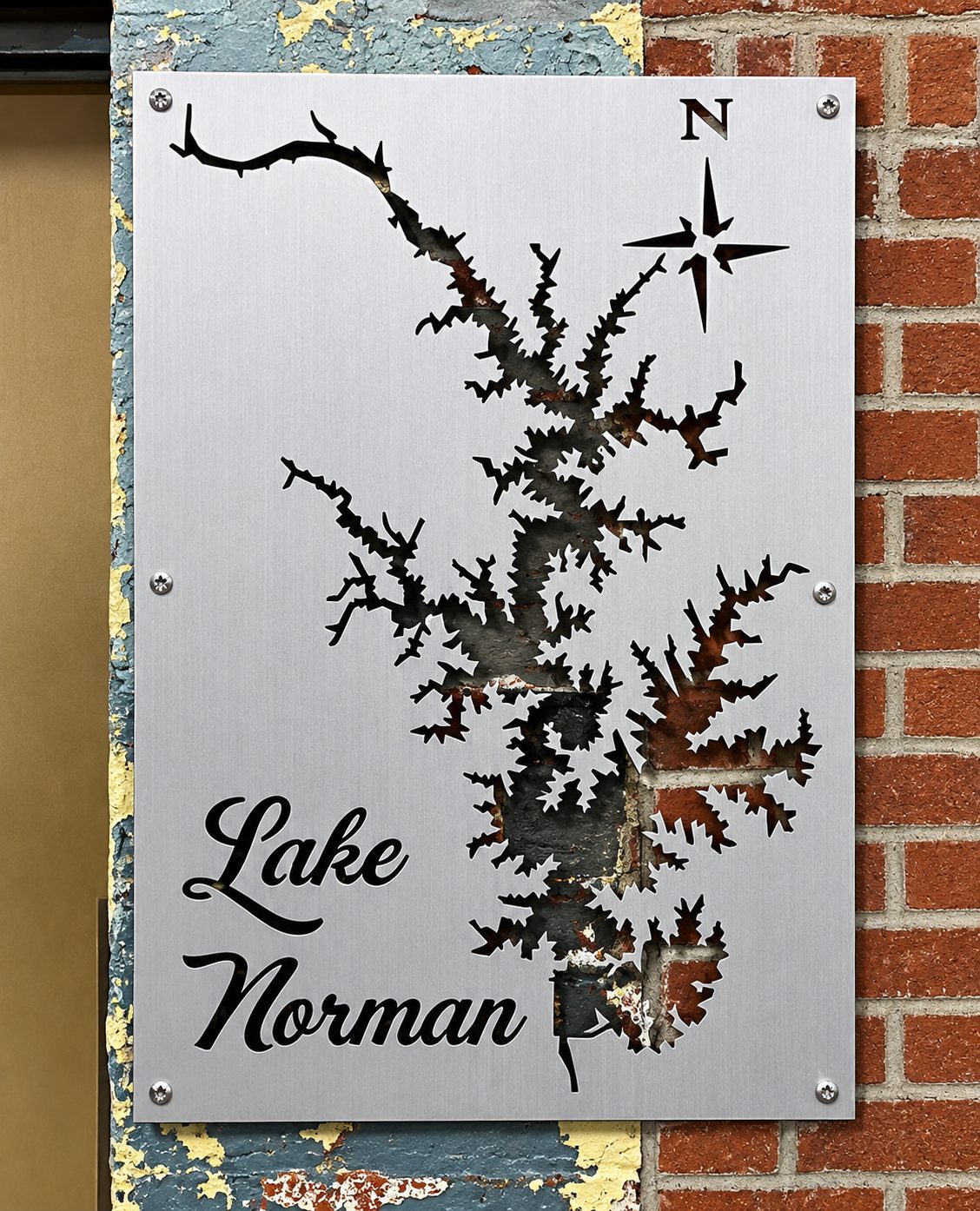 Lake Norman brushed metal map with open shoreline cutouts, displayed against a brick wall.
